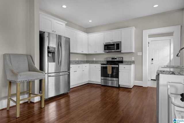 kitchen with appliances with stainless steel finishes, white cabinetry, light stone counters, a sink, and dark wood-style floors