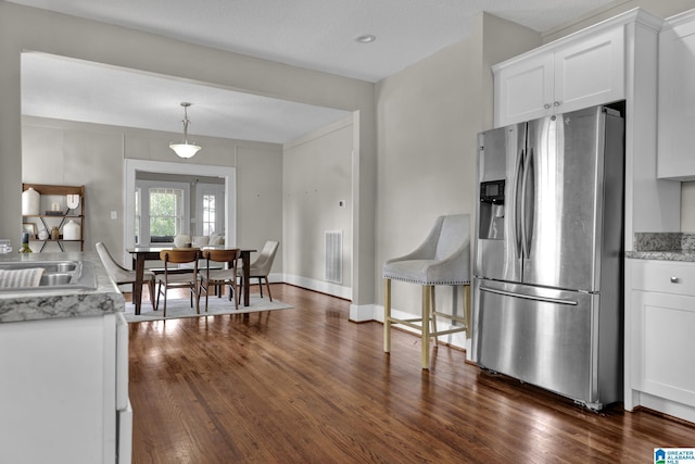 kitchen featuring stainless steel fridge with ice dispenser, dark wood-type flooring, white cabinets, a sink, and decorative light fixtures