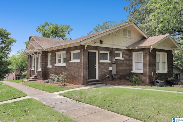 view of front of property with entry steps, a front lawn, brick siding, and a shingled roof