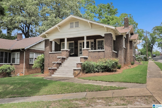 view of front of house with brick siding, a front lawn, a chimney, and a porch