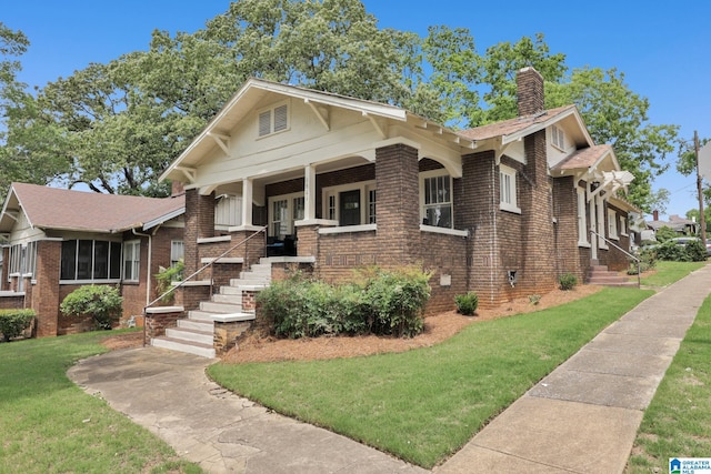 view of front of house with a chimney, a front yard, brick siding, and a porch