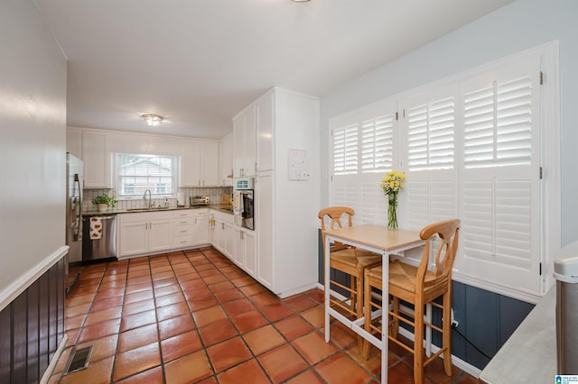 3309 Eaton Rd, Mountain Brook, AL 35223 - kitchen with appliances with stainless steel finishes, a sink, decorative backsplash, white cabinetry, and light tile patterned floors