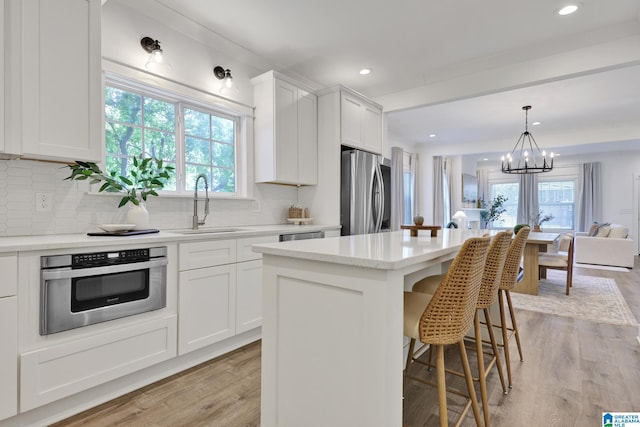 1505 36th St N, Birmingham, AL 35234 - kitchen featuring appliances with stainless steel finishes, a sink, a chandelier, light wood-style flooring, and tasteful backsplash