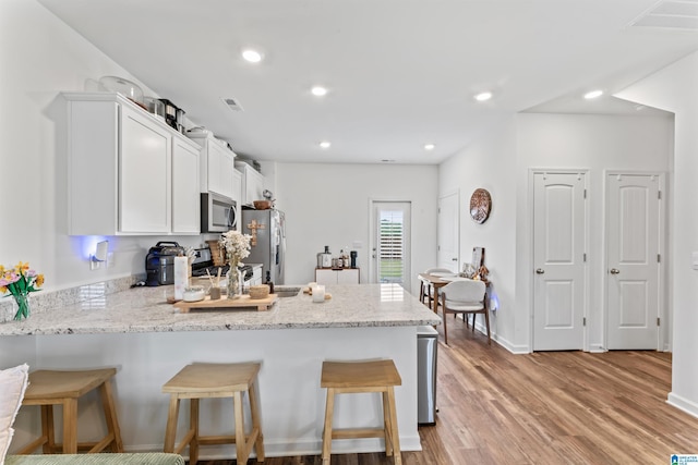 1063 Archers Trl E, Springville, AL 35146 - kitchen featuring appliances with stainless steel finishes, a peninsula, white cabinetry, light wood finished floors, and a kitchen breakfast bar