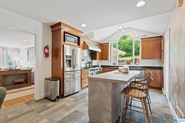 3208 N Woodridge Rd, Mountain Brook, AL 35223 - kitchen with stainless steel appliances, plenty of natural light, stone tile flooring, a kitchen bar, and vaulted ceiling