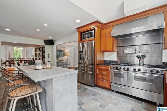 3208 N Woodridge Rd, Mountain Brook, AL 35223 - kitchen with stainless steel appliances, wall chimney range hood, a kitchen breakfast bar, recessed lighting, and brown cabinets