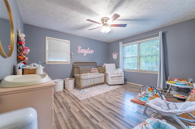 1214 Wildoak Dr, Anniston, AL 36206 - bedroom featuring wood finished floors, a textured ceiling, a crib, a ceiling fan, and baseboards
