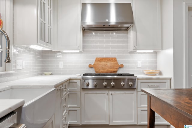 409 Euclid Ave, Mountain Brook, AL 35213 - kitchen featuring wall chimney range hood, stainless steel gas cooktop, backsplash, a sink, and white cabinets