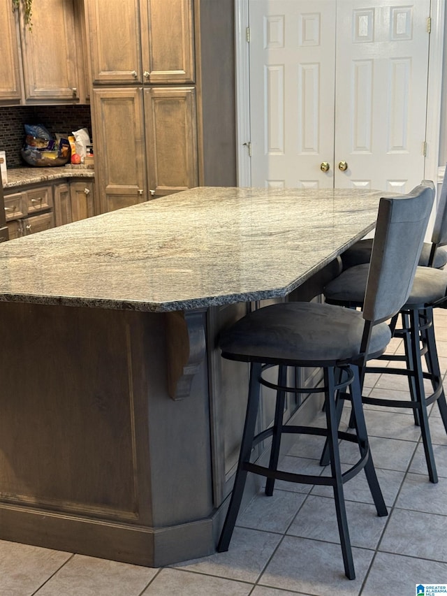 5616 Elliott Cir, Mccalla, AL 35111 - kitchen with light tile patterned floors, light stone countertops, a breakfast bar area, and tasteful backsplash