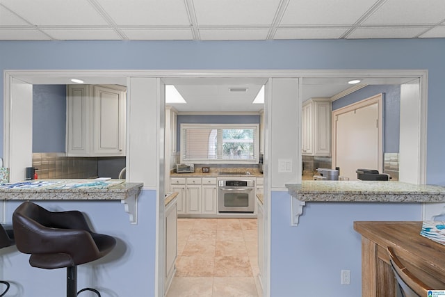 200 Asphodel Dr, Dothan, AL 36303 - kitchen featuring oven, a breakfast bar, a drop ceiling, backsplash, and light tile patterned flooring