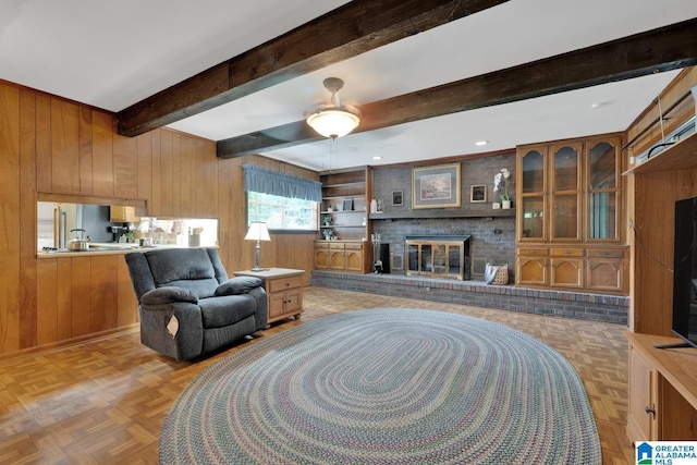 5420 Pine St, Sylvan Springs, AL 35118 - living room featuring wooden walls, beam ceiling, a brick fireplace, and a ceiling fan