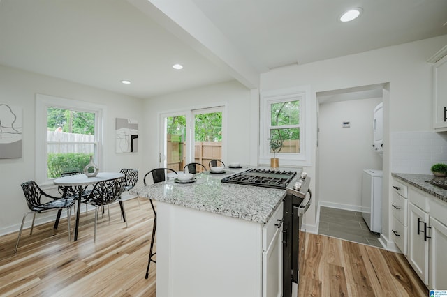 1751 Valley Ave Unit D, Homewood, AL 35209 - kitchen with stainless steel gas stove, a breakfast bar area, light wood-style floors, stacked washing machine and dryer, and plenty of natural light