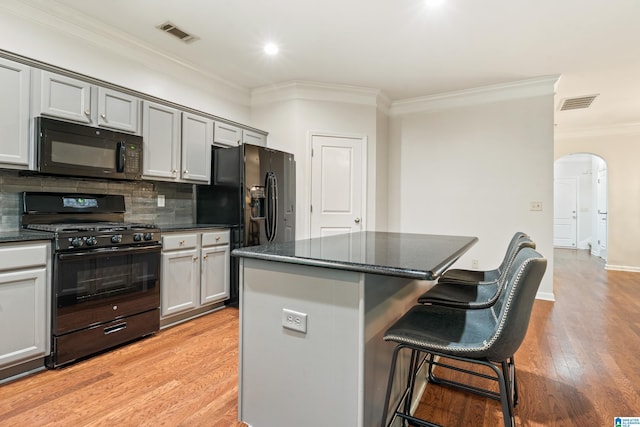 1033 Inverness Cove Way, Hoover, AL 35242 - kitchen featuring black appliances, arched walkways, crown molding, a center island, and a kitchen bar