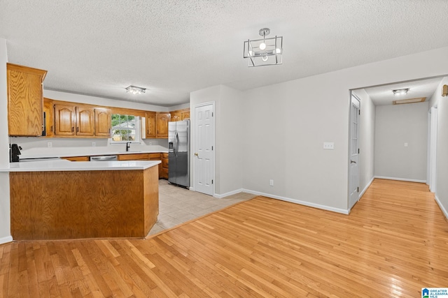 6415 Mays Bend Rd, Pell City, AL 35128 - kitchen featuring appliances with stainless steel finishes, light wood finished floors, a peninsula, a textured ceiling, and brown cabinetry