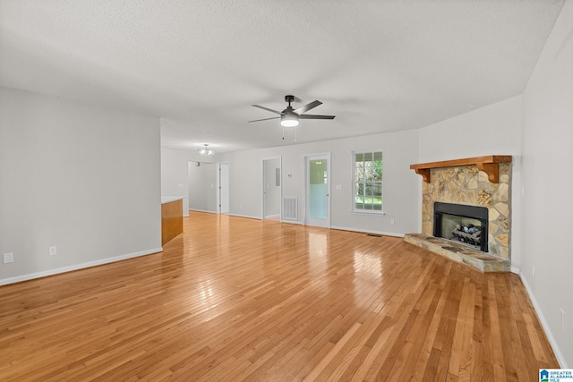 6415 Mays Bend Rd, Pell City, AL 35128 - unfurnished living room with light wood-style flooring, a stone fireplace, ceiling fan, baseboards, and a textured ceiling