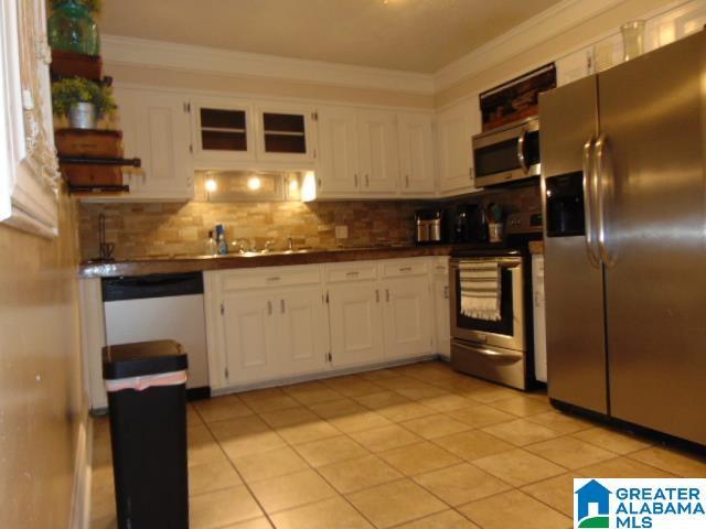101 Randall Cir, Clanton, AL 35045 - kitchen with appliances with stainless steel finishes, white cabinetry, light tile patterned floors, tasteful backsplash, and ornamental molding