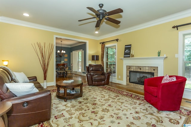5668 Carrington Lake Pkwy, Trussville, AL 35173 - living room featuring ornamental molding, a chandelier, a tiled fireplace, ceiling fan, and wood finished floors