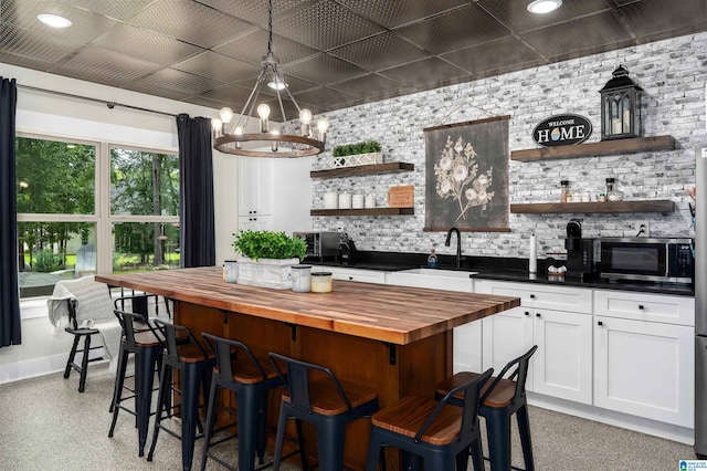 715 W Cassie Dr, Pell City, AL 35128 - kitchen with butcher block countertops, open shelves, stainless steel microwave, white cabinets, and a chandelier