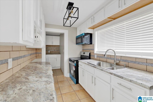 1125 SW 15th St, Birmingham, AL 35211 - kitchen with stainless steel range with electric stovetop, black microwave, decorative backsplash, white cabinetry, and light tile patterned flooring