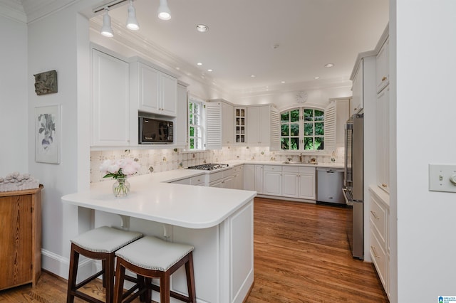 101 Mountain Ave, Mountain Brook, AL 35213 - kitchen featuring appliances with stainless steel finishes, a peninsula, crown molding, backsplash, and wood finished floors
