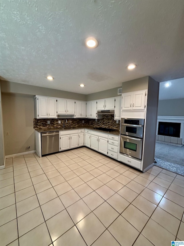 1221 Dalraida Rd, Montgomery, AL 36109 - kitchen with appliances with stainless steel finishes, dark countertops, decorative backsplash, under cabinet range hood, and white cabinetry