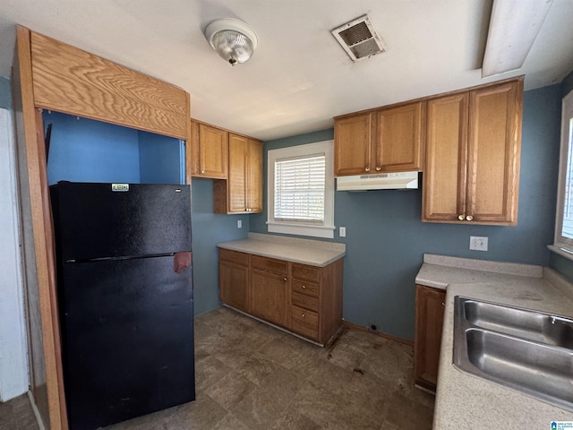 319 Lapsley Ave, Anniston, AL 36207 - kitchen featuring freestanding refrigerator, brown cabinetry, under cabinet range hood, and light countertops