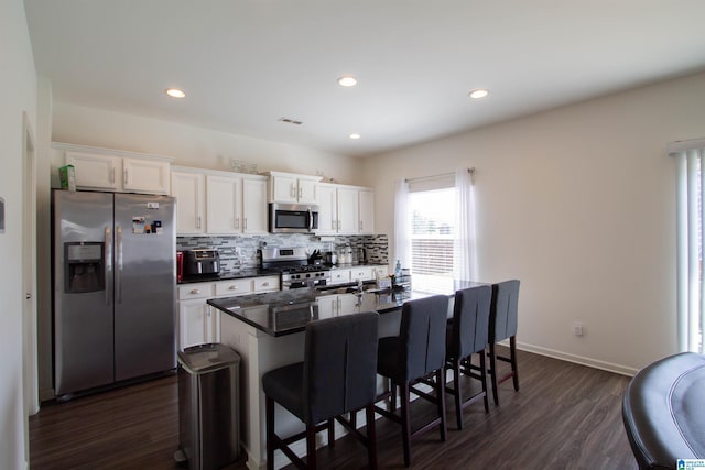 6497 Newbridge Dr, Bessemer, AL 35022 - kitchen with stainless steel appliances, dark countertops, an island with sink, tasteful backsplash, and dark wood-style floors