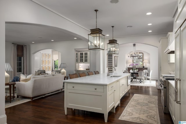 3600 Park Ln S, Mountain Brook, AL 35213 - kitchen with stainless steel stove, arched walkways, white cabinets, ornamental molding, and a kitchen island with sink