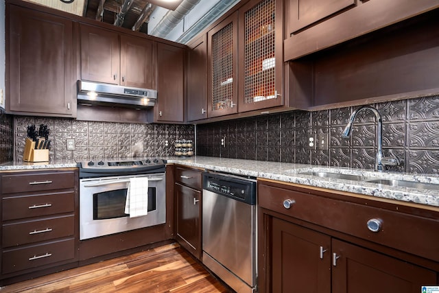 2217 2nd Ave Unit 303, Birmingham, AL 35203 - kitchen featuring stainless steel appliances, under cabinet range hood, light stone countertops, light wood-type flooring, and glass insert cabinets