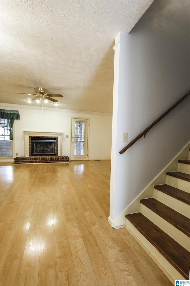1534 Cambridge Pl, Anniston, AL 36207 - unfurnished living room with ceiling fan, a textured ceiling, light wood-style flooring, a brick fireplace, and stairway