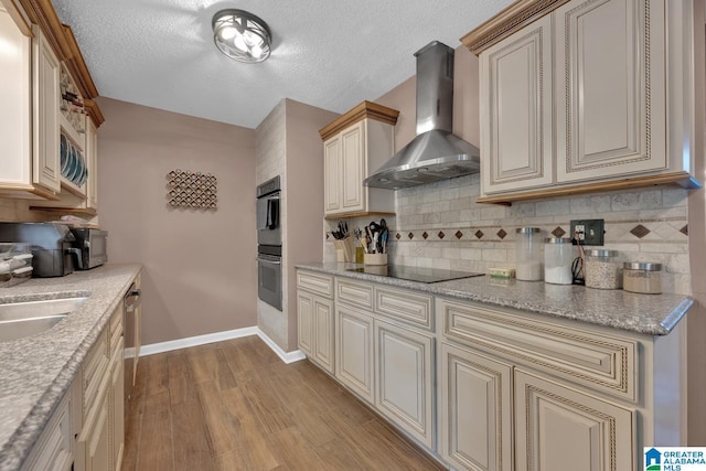 1025 Old Section Rd, Hoover, AL 35244 - kitchen with wall chimney range hood, cream cabinets, light wood-style floors, stainless steel double oven, and a textured ceiling