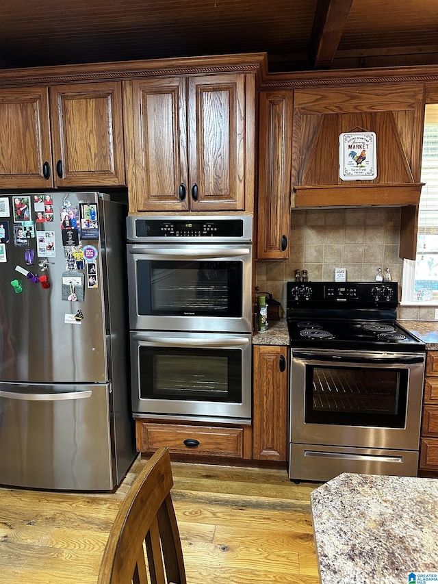76 Goggins Dr, Montevallo, AL 35115 - kitchen featuring appliances with stainless steel finishes, light wood finished floors, exhaust hood, brown cabinetry, and decorative backsplash
