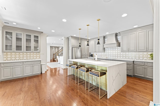 5615 Canongate Ln, Hoover, AL 35242 - kitchen with custom exhaust hood, gray cabinets, a kitchen island with sink, a breakfast bar, and decorative backsplash