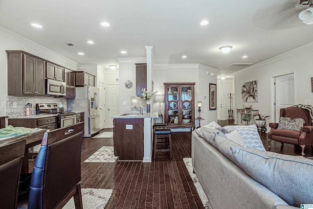 4955 Stonecreek Way, Calera, AL 35040 - kitchen featuring appliances with stainless steel finishes, open floor plan, a breakfast bar, dark brown cabinetry, and ornamental molding
