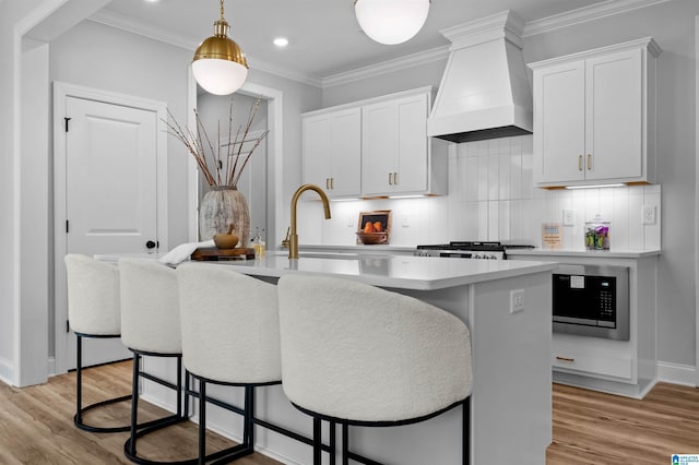 200 Simms Lndg, Pelham, AL 35124 - kitchen featuring premium range hood, a center island with sink, decorative backsplash, light wood finished floors, and light countertops