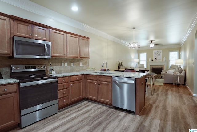 1186 Inverness Cove Way, Hoover, AL 35242 - kitchen featuring appliances with stainless steel finishes, a peninsula, light wood-type flooring, a fireplace, and decorative backsplash