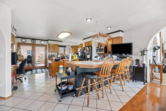 interior space featuring an inviting chandelier, light tile floors, a kitchen breakfast bar, kitchen peninsula, and black fridge