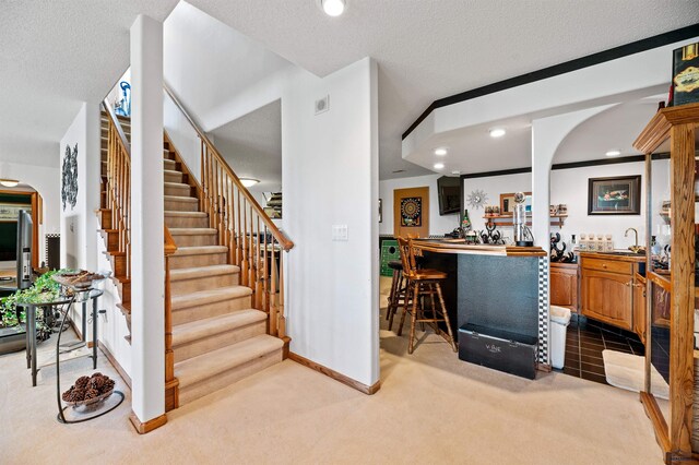 staircase featuring light carpet, a textured ceiling, and crown molding