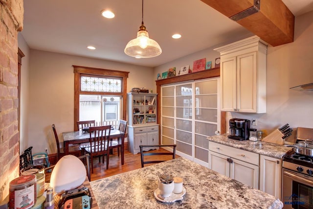 kitchen with light stone counters, stove, brick wall, hardwood / wood-style floors, and hanging light fixtures