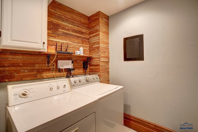 clothes washing area featuring washer and clothes dryer, wooden walls, and cabinets