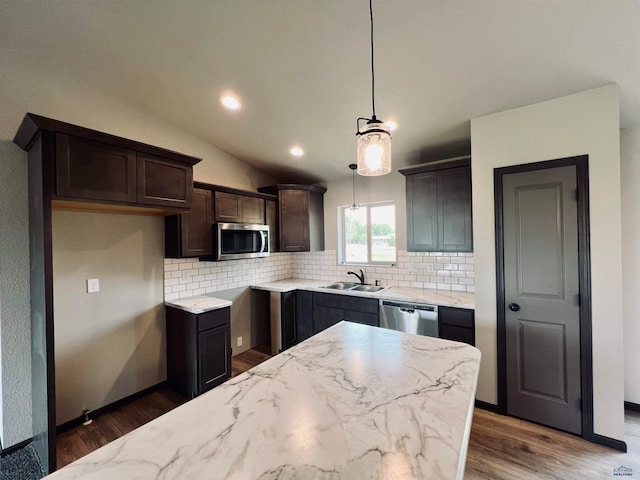 kitchen with appliances with stainless steel finishes, vaulted ceiling, tasteful backsplash, dark hardwood / wood-style flooring, and pendant lighting