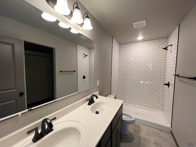 bathroom featuring toilet, tiled shower, vanity with extensive cabinet space, dual sinks, and tile flooring