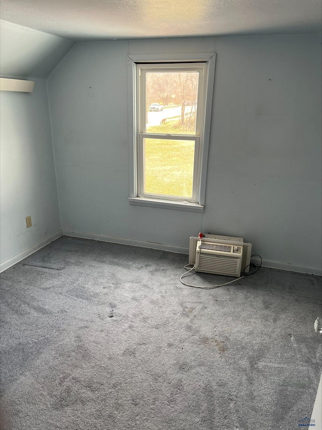 carpeted spare room with a wall mounted air conditioner, vaulted ceiling, and a textured ceiling