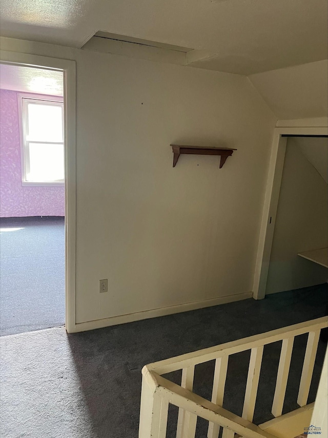 stairs with dark colored carpet, vaulted ceiling, and a textured ceiling