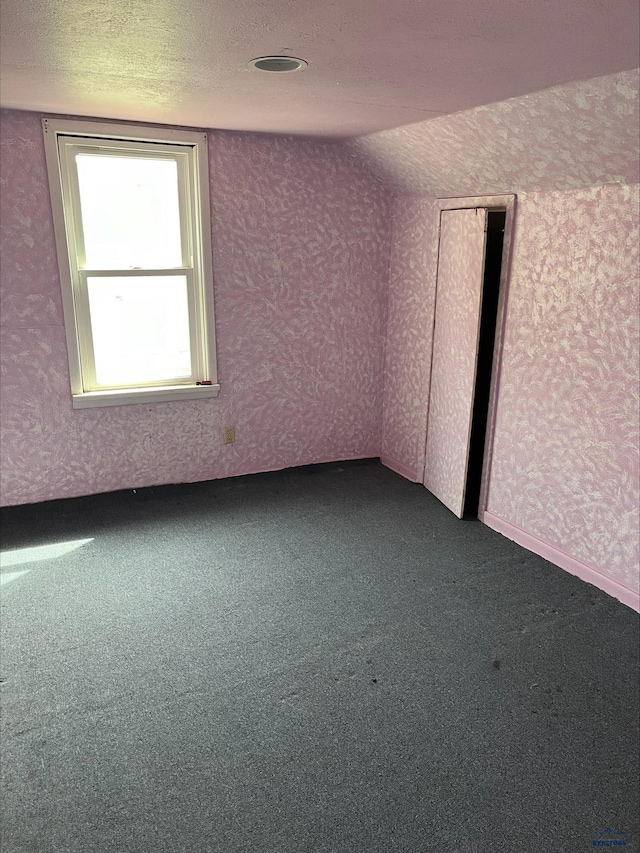 unfurnished room with lofted ceiling, dark carpet, and a textured ceiling