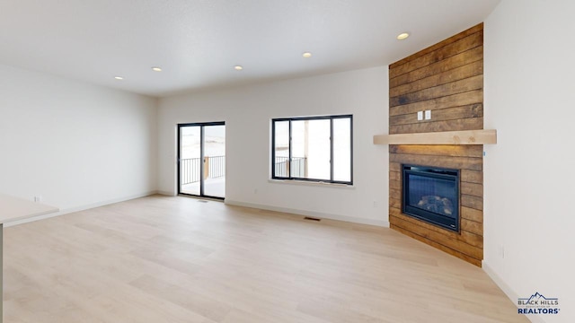 unfurnished living room featuring light hardwood / wood-style floors, wooden walls, and a large fireplace