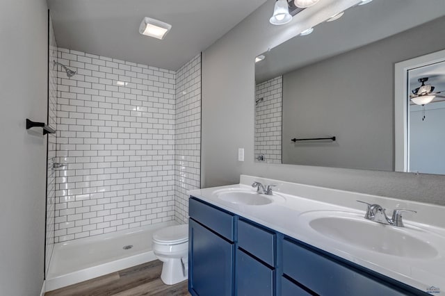 bathroom with double sink vanity, ceiling fan, a tile shower, toilet, and hardwood / wood-style flooring