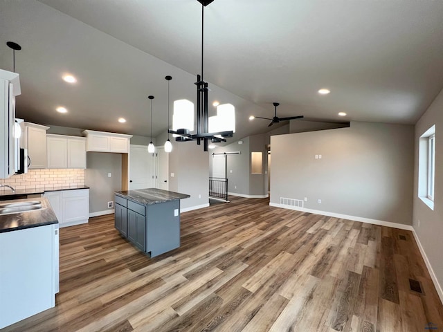 kitchen with pendant lighting, light wood-type flooring, white cabinetry, vaulted ceiling, and a kitchen island