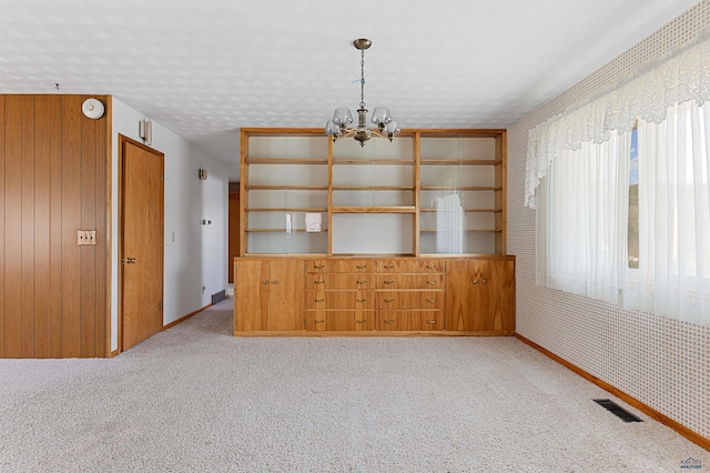 unfurnished dining area featuring an inviting chandelier, a textured ceiling, and carpet floors