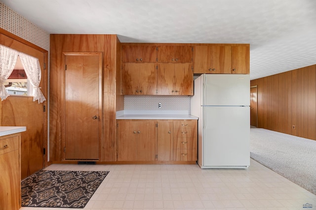 kitchen with white refrigerator, backsplash, light tile floors, and wooden walls